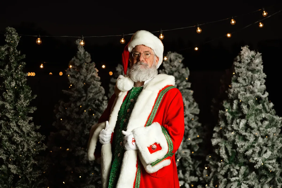 Santa Michael in his red velvet coat, standing in a snowy Christmas-tree setting.